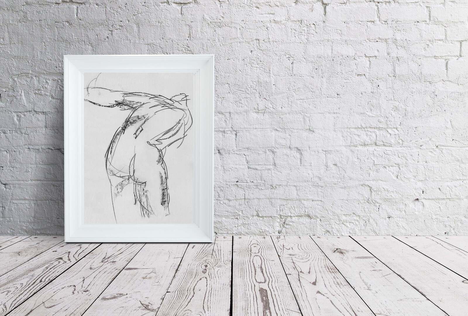 Charcoal female figure sketch framed and sitting on distressed wood floor leaning on a white brick wall