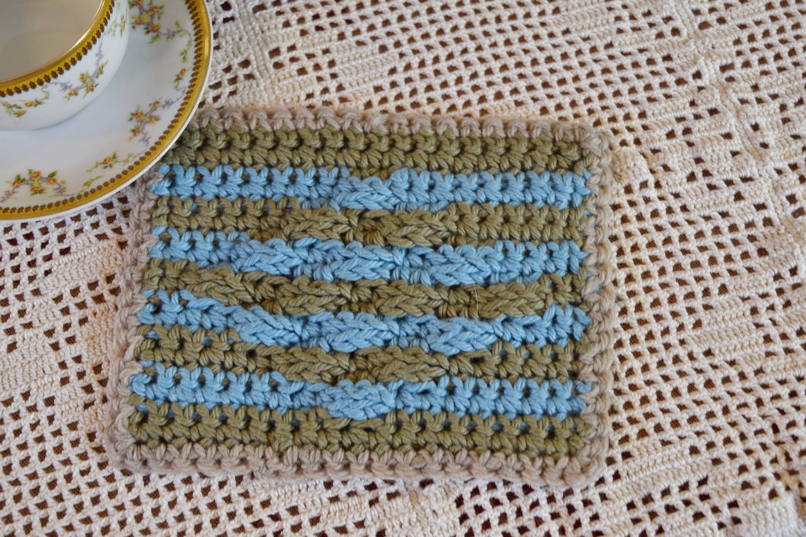 Crochet potholder sitting on a filet crochet tablecloth