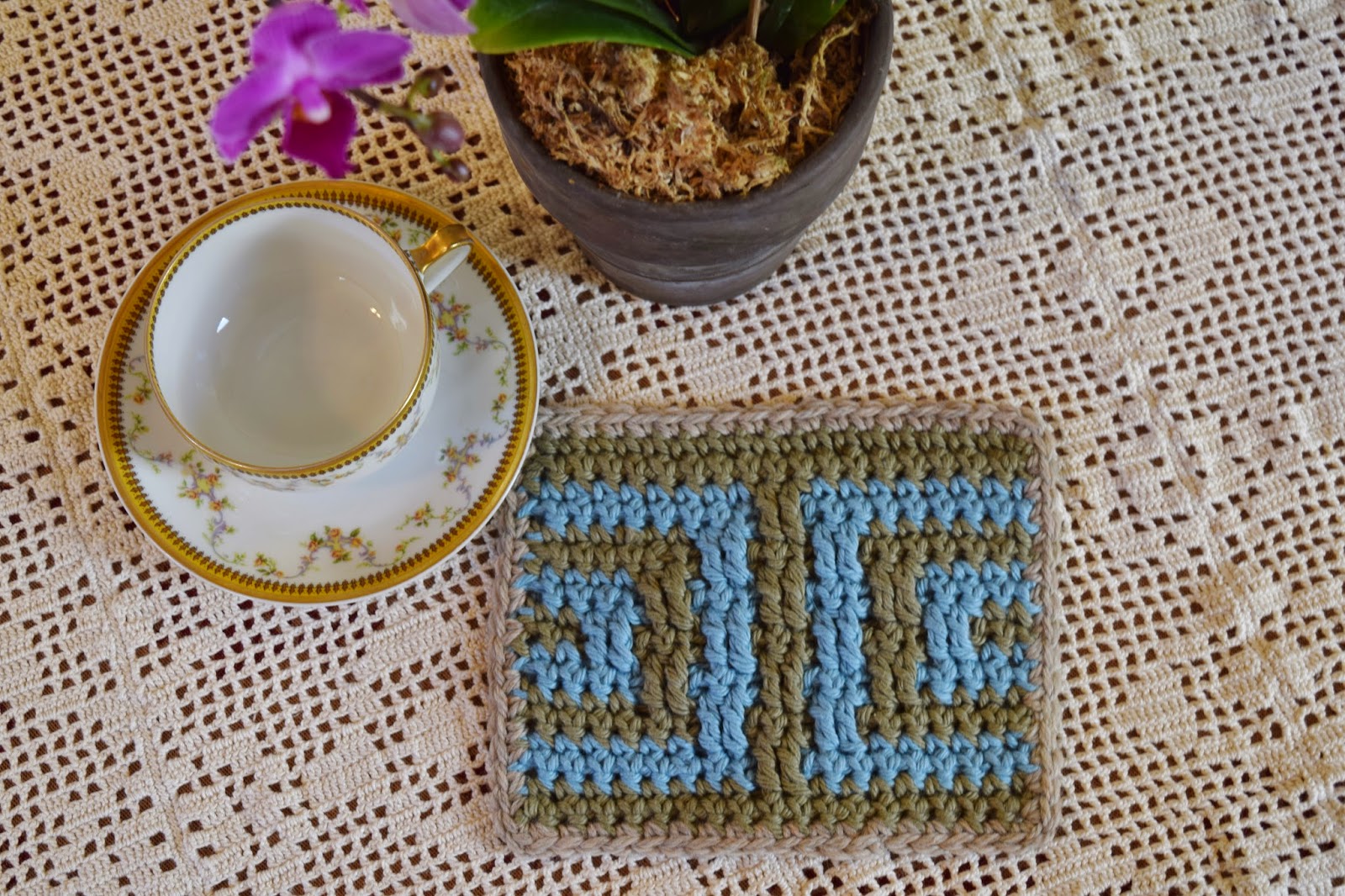 Crochet potholder sitting on a filet crochet tablecloth