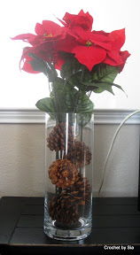 Poinsettias in glass vase filled with pinecones